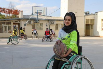 A girl with a disability is holding a basketball.