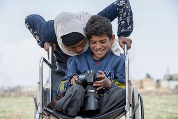 A boy with a disability is playing with a camera.